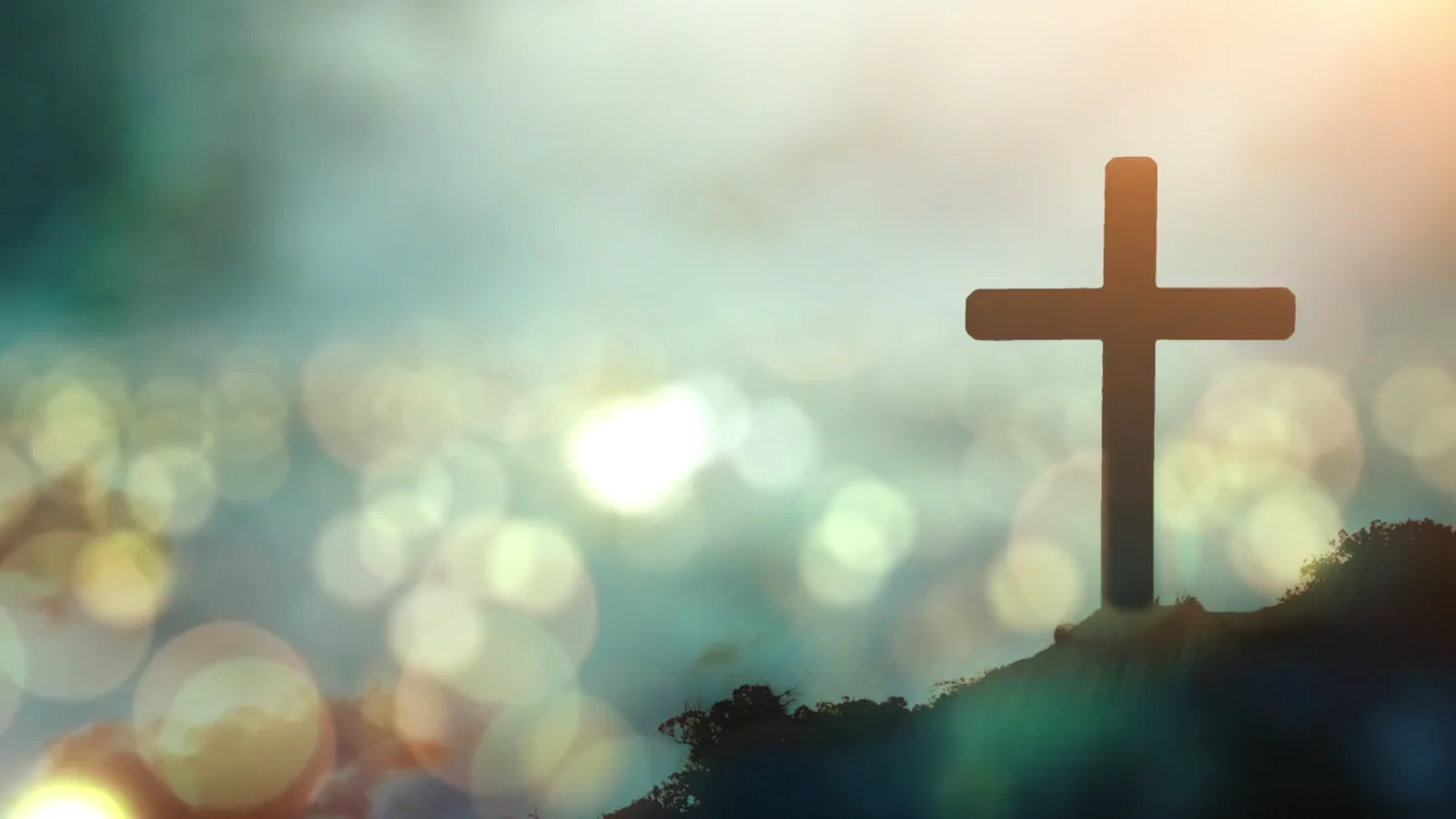 Wooden cross silhouetted on hillside against blurred sky with bokeh lights