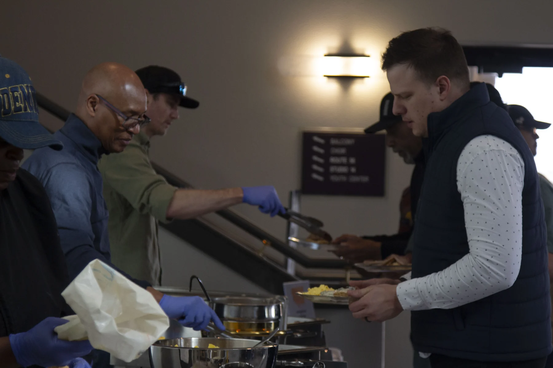 People serving and receiving food at an indoor catering or community event