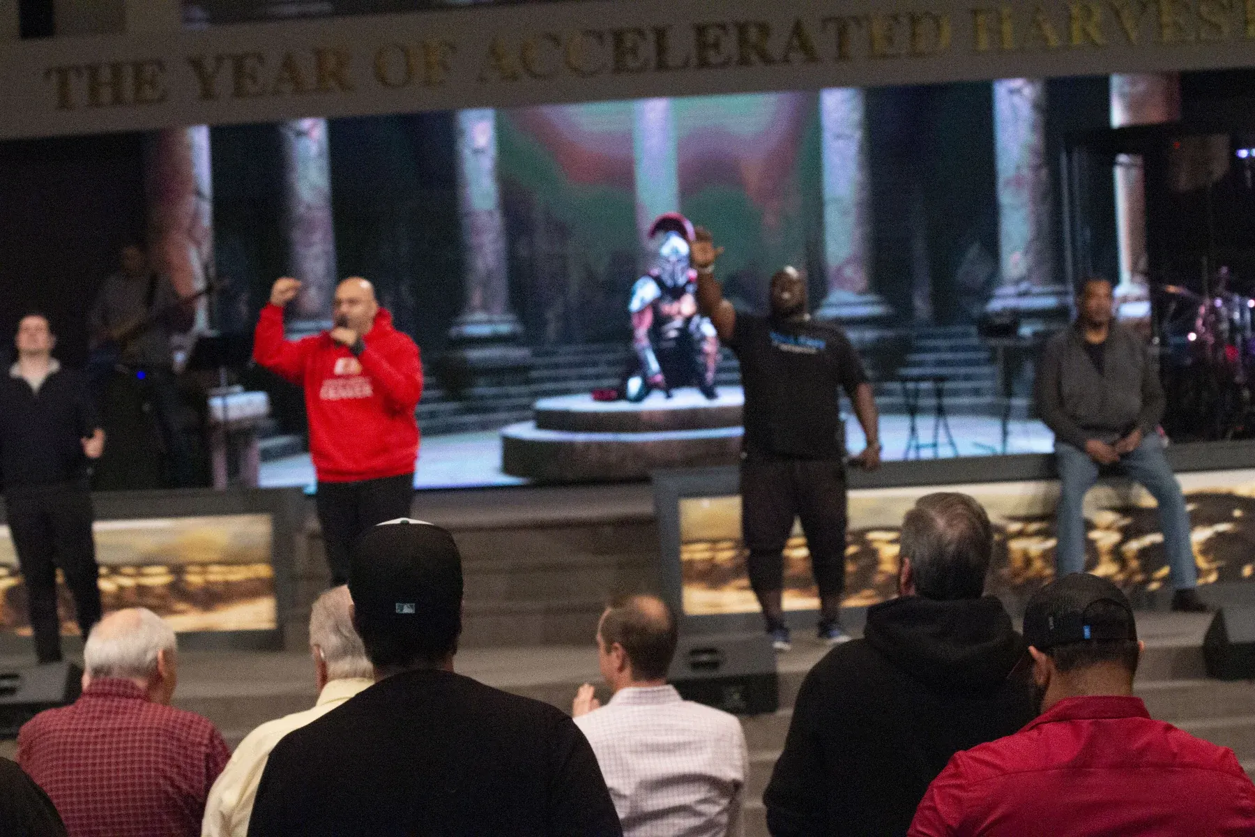 Audience members watch a stage presentation with performers and classical architecture backdrop