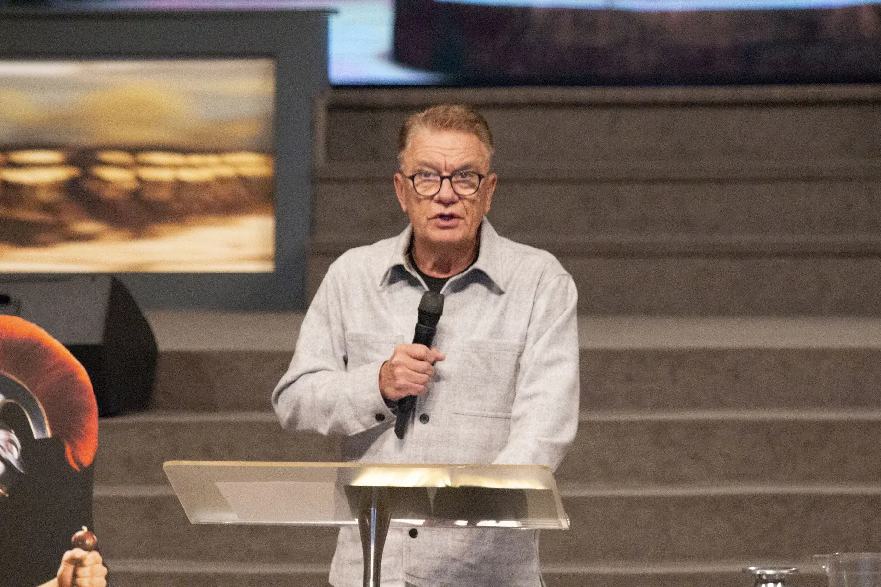 Man in glasses speaking at podium with microphone in modern auditorium