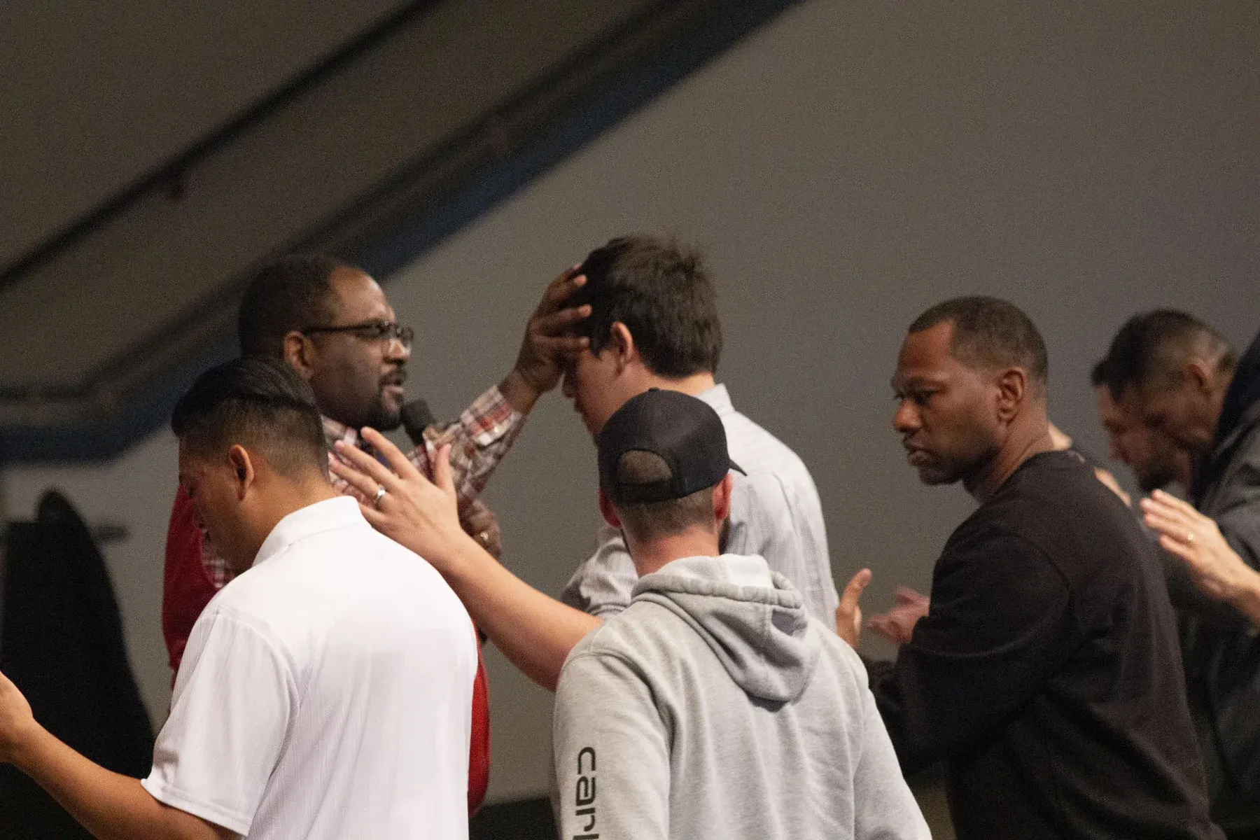 Group of men in casual attire engaged in discussion and prayer at an indoor event