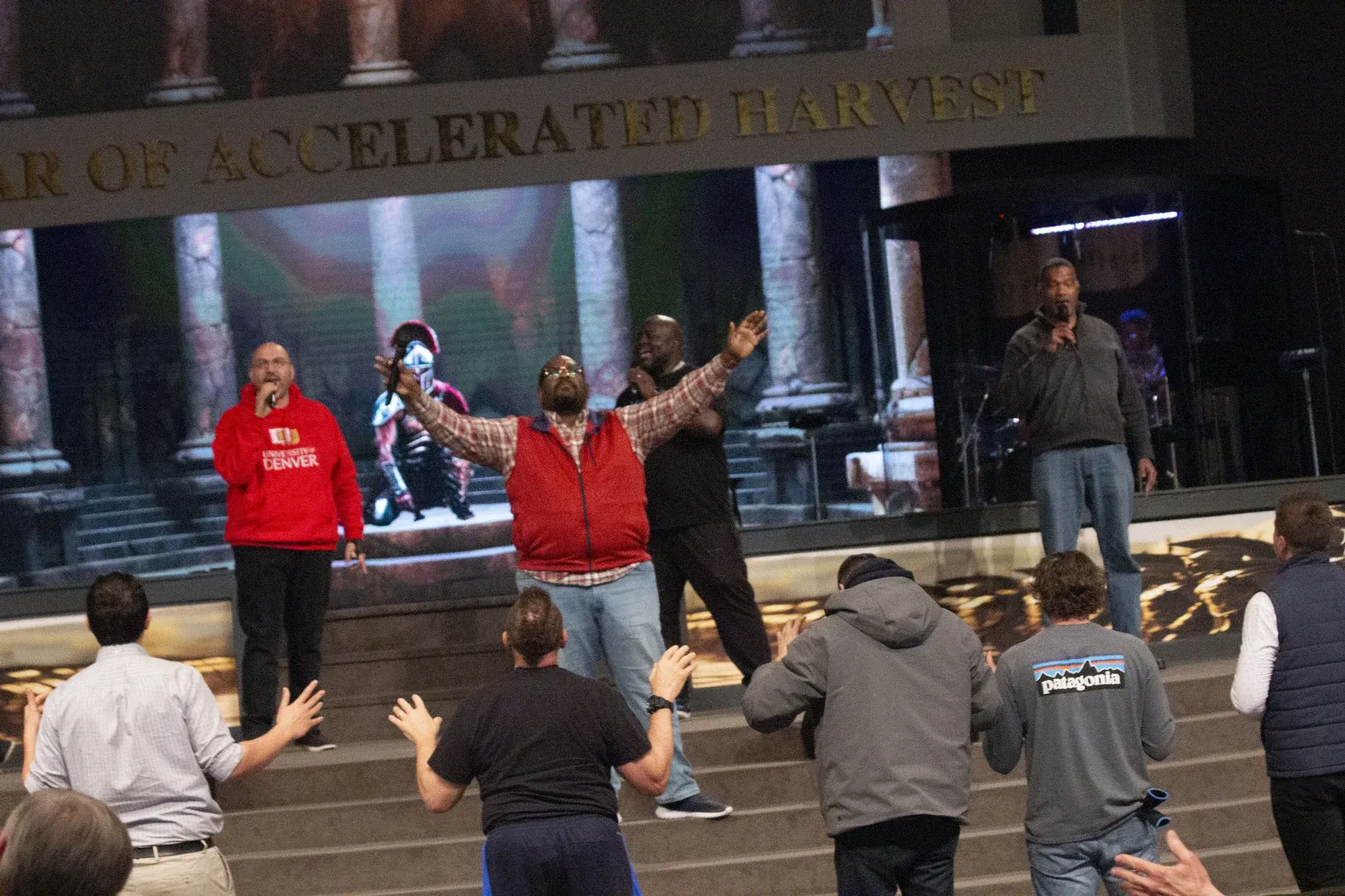 Group of people gathered on steps at indoor event with performers on stage